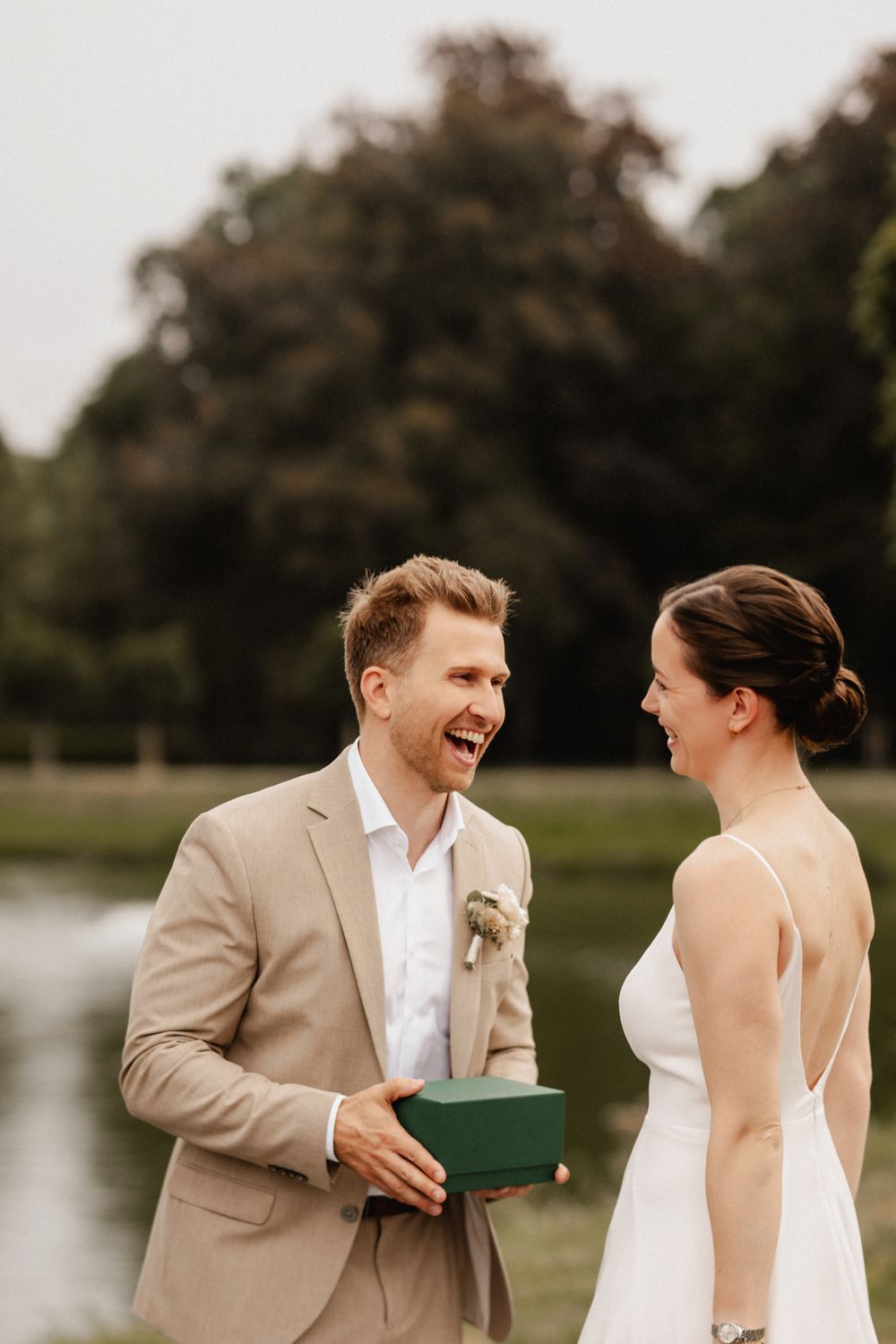 A couple shares a joyful moment together during their wedding photoshoot by a lake.