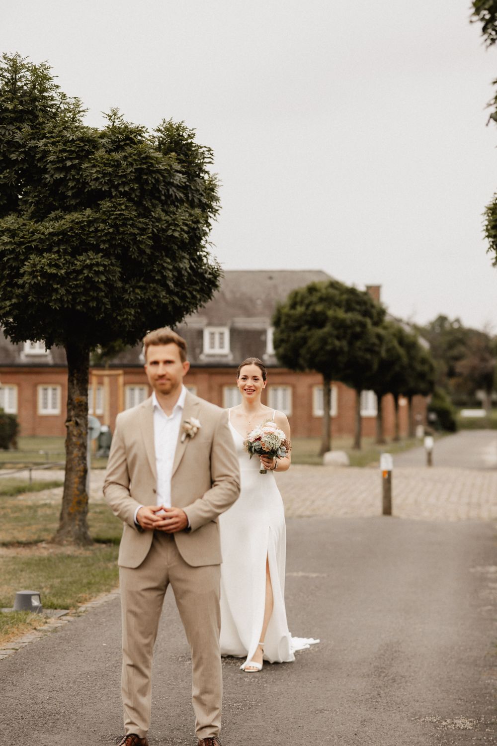A wedding couple poses playfully on a tree-lined country road in warm autumn light.