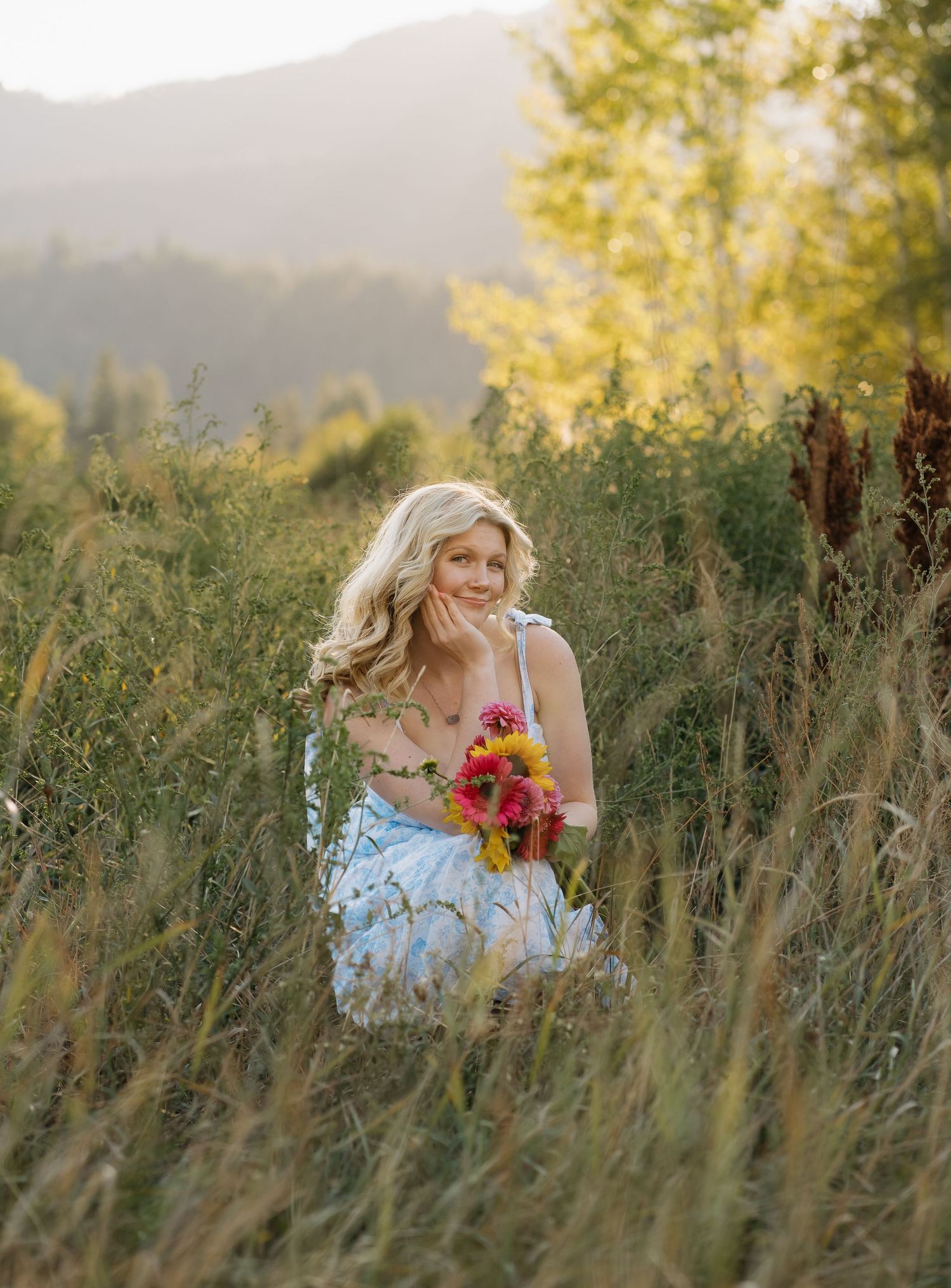 Person in floral dress holding colorful bouquet in mountain meadow at sunset.