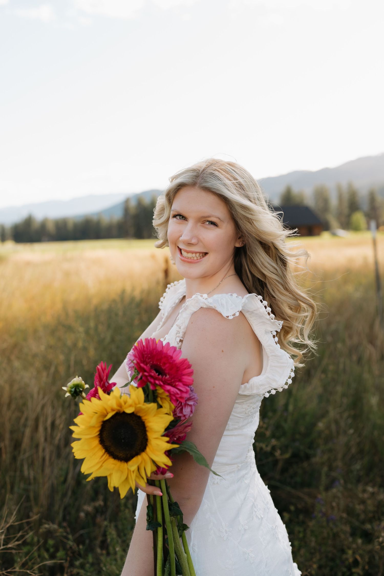 Person in white lace dress holding sunflowers against mountain landscape.