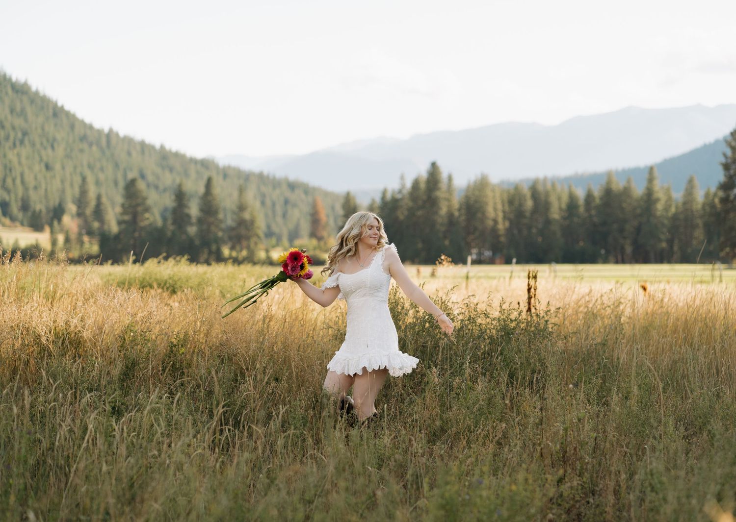 Person in white dress twirling with flowers in mountain meadow at sunset.