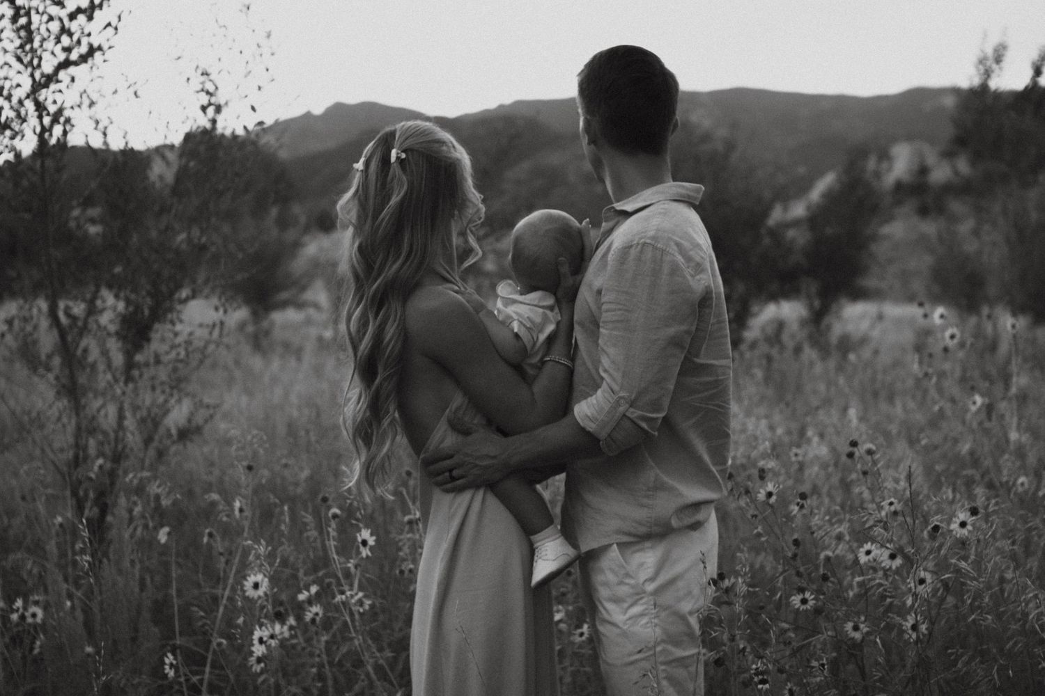 A series of romantic black and white photos showing a couple embracing in a wildflower meadow at sunset.