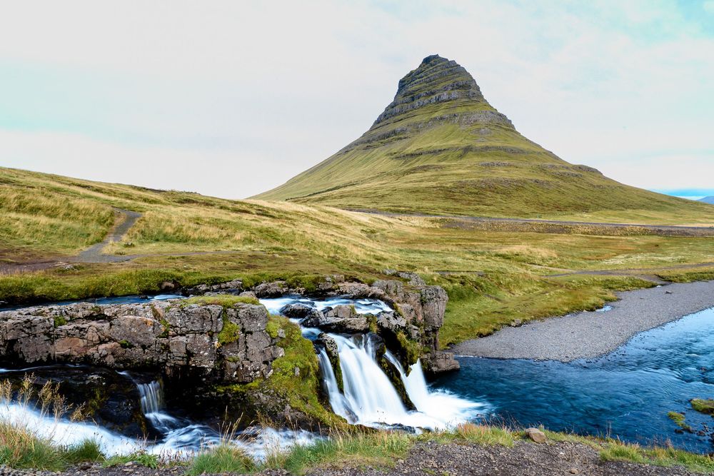 Scenic Kirkjufell mountain with cascading waterfall in foreground and green landscape in Iceland.