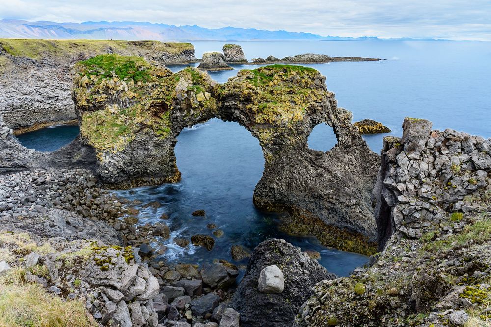 Rocky coastal tidepools with clear blue water and seaweed along a rugged shoreline on a sunny day.