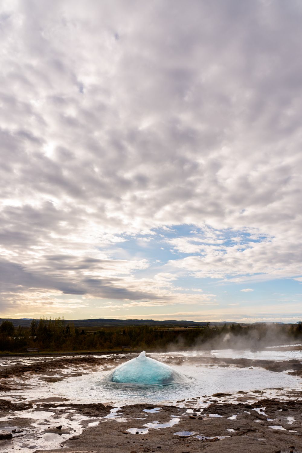 Snow-covered landscape with steaming geothermal features and dramatic cloud formations at Yellowstone National Park.