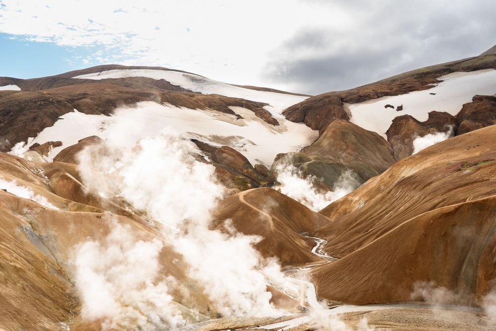 Panoramic view of snow-covered mountains with brown rocky terrain and cloudy skies in Iceland's highlands.