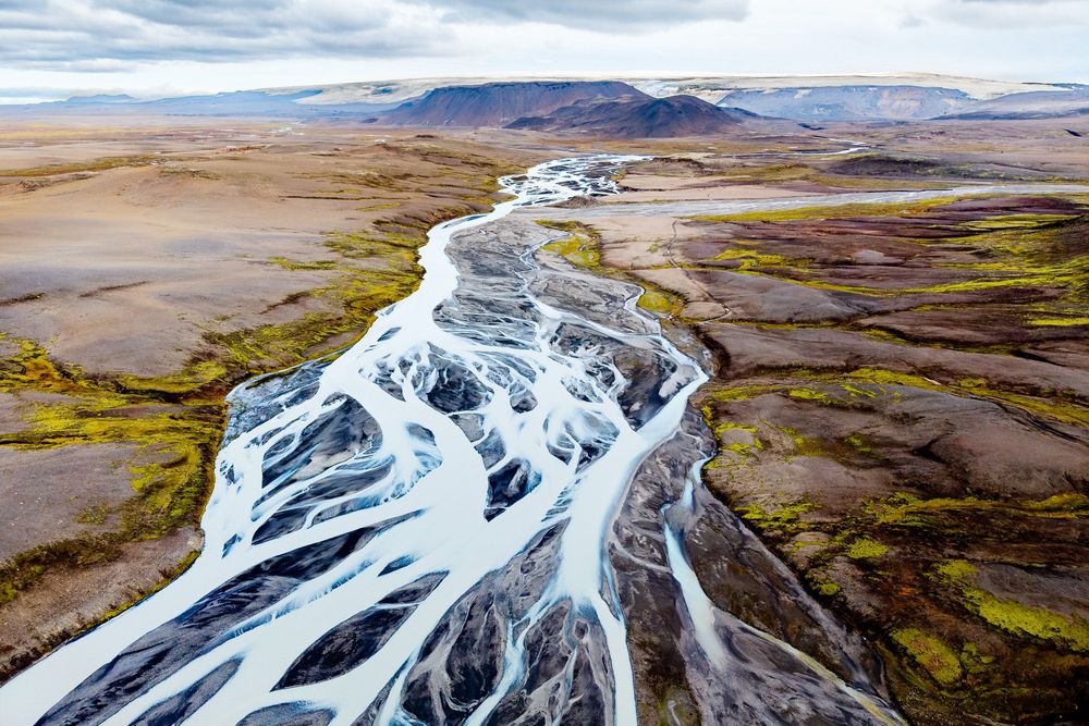 Aerial view of braided glacial rivers creating intricate patterns across Icelandic landscape in dramatic light.