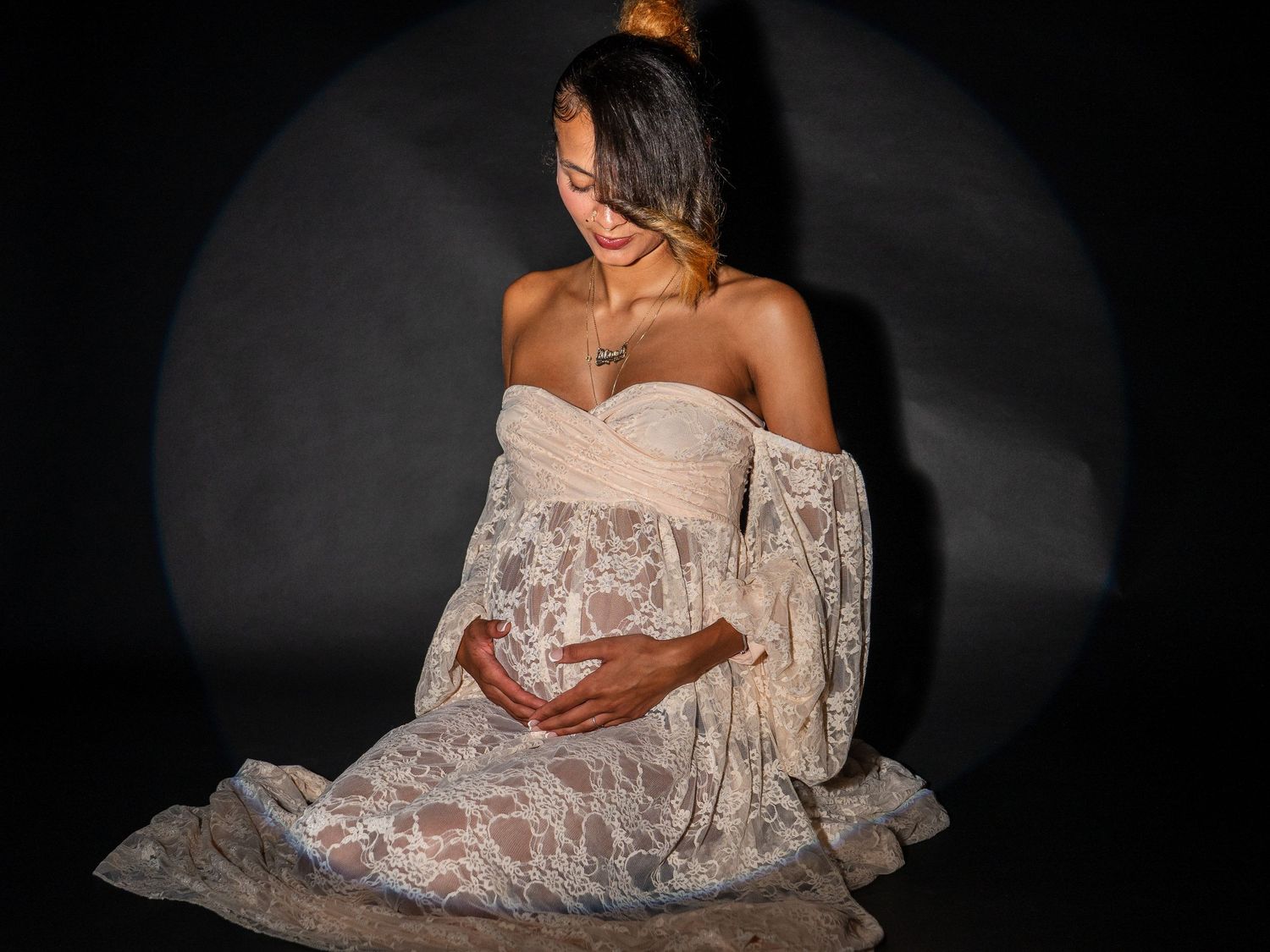 Artistic maternity photo series showing a pregnant woman in white lace dress against dark background.
