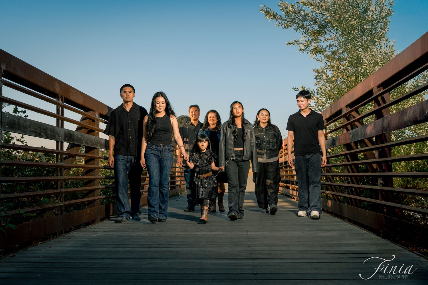 A group stands together on a wooden bridge during golden hour with trees and blue sky in the background.