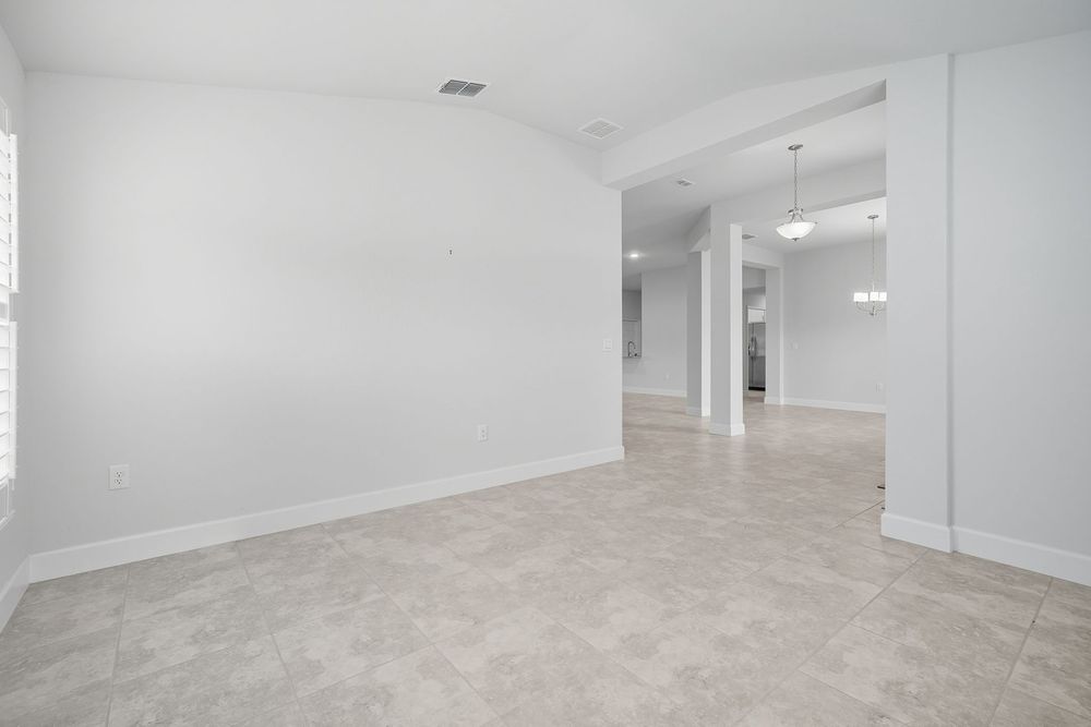 Open concept interior space with neutral tile flooring, white walls and recessed lighting leading to other rooms.