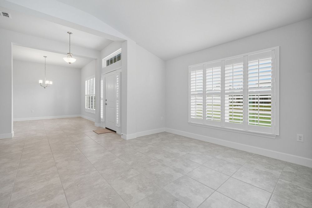 Modern white interior room with plantation shutters, crown molding, and light gray flooring throughout.