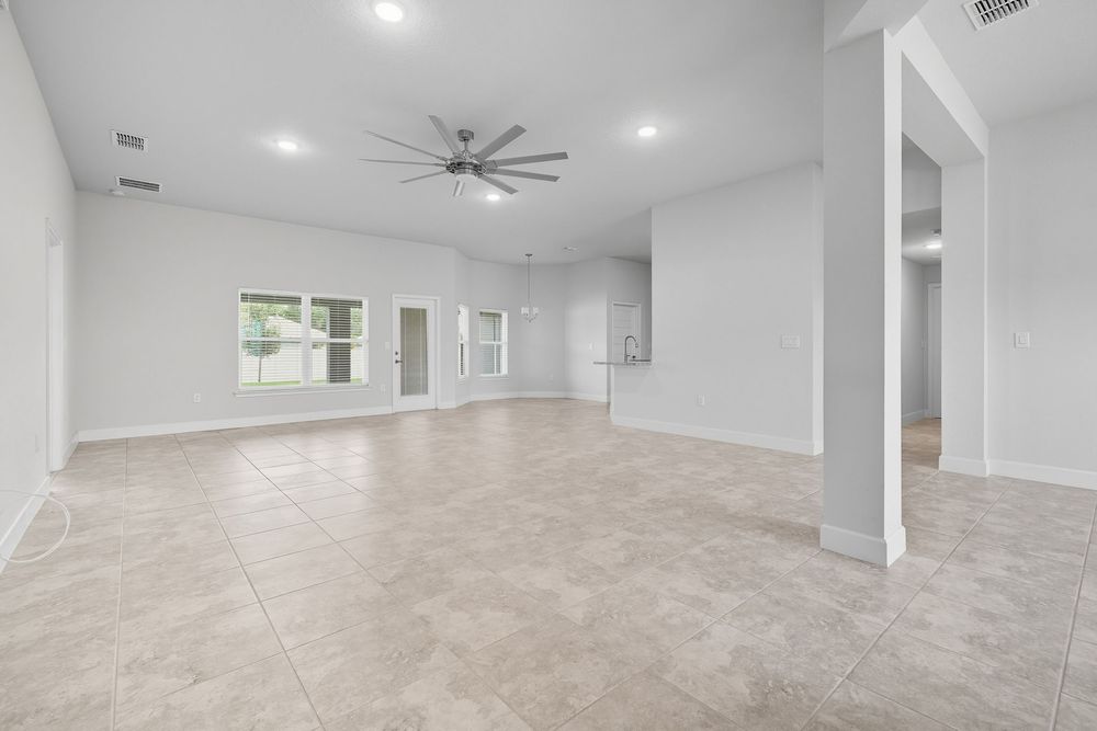 Empty modern living room interior with beige tile flooring, white walls, recessed lighting and ceiling fan.