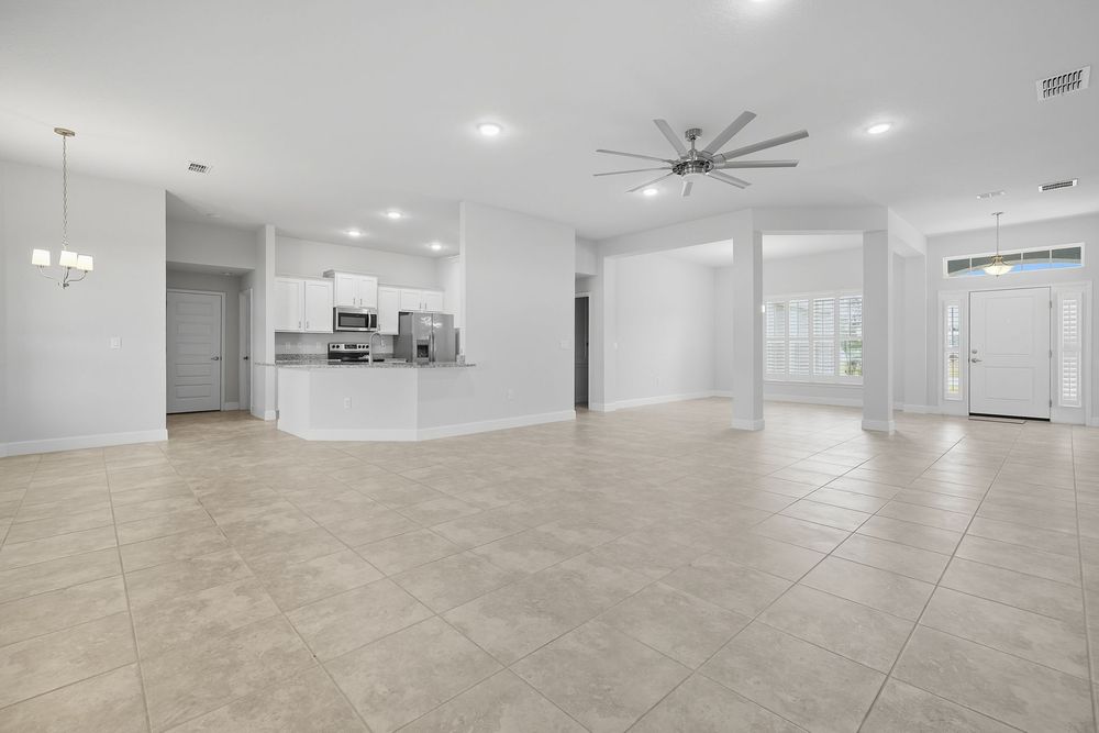 Modern open concept living space with beige tile floors, white walls, and a large ceiling fan in a bright empty room.