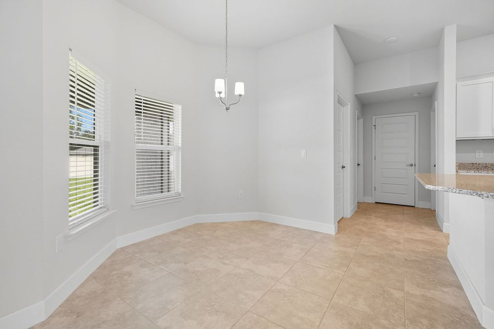 Modern white kitchen with sleek cabinets, quartz countertops, and hardwood floors opens to a bright dining area.