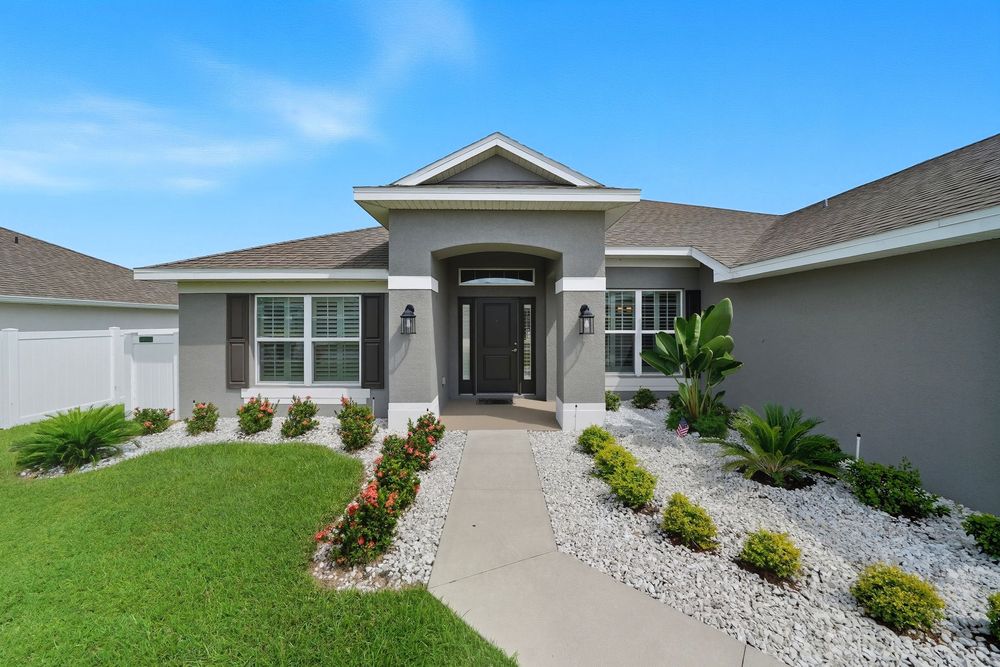A modern single-story home exterior with landscaped garden beds and white rock accents along the facade.