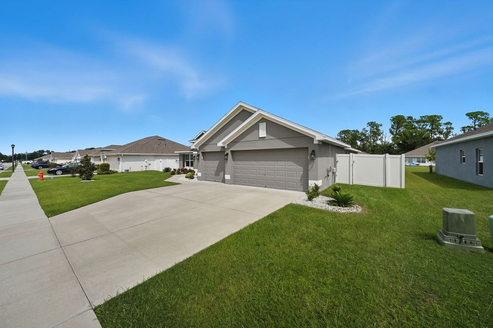 Concrete driveway leading to a residential garage with green lawn on both sides under blue sky.