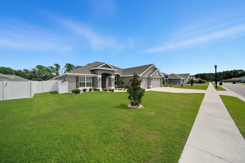 Single-story ranch home with beige exterior and well-maintained green lawn along concrete sidewalk under blue sky.