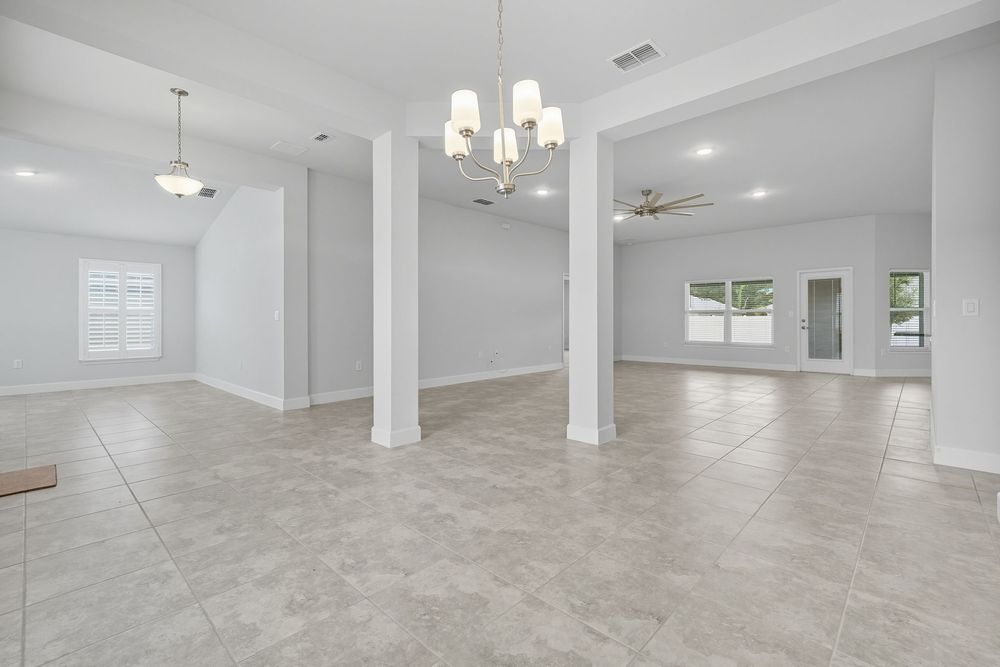 Modern open concept living space with white walls, beige tile floors, and elegant chandelier lighting.