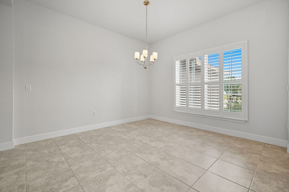 Modern empty room with beige tile floors, white walls and a large window with plantation shutters.