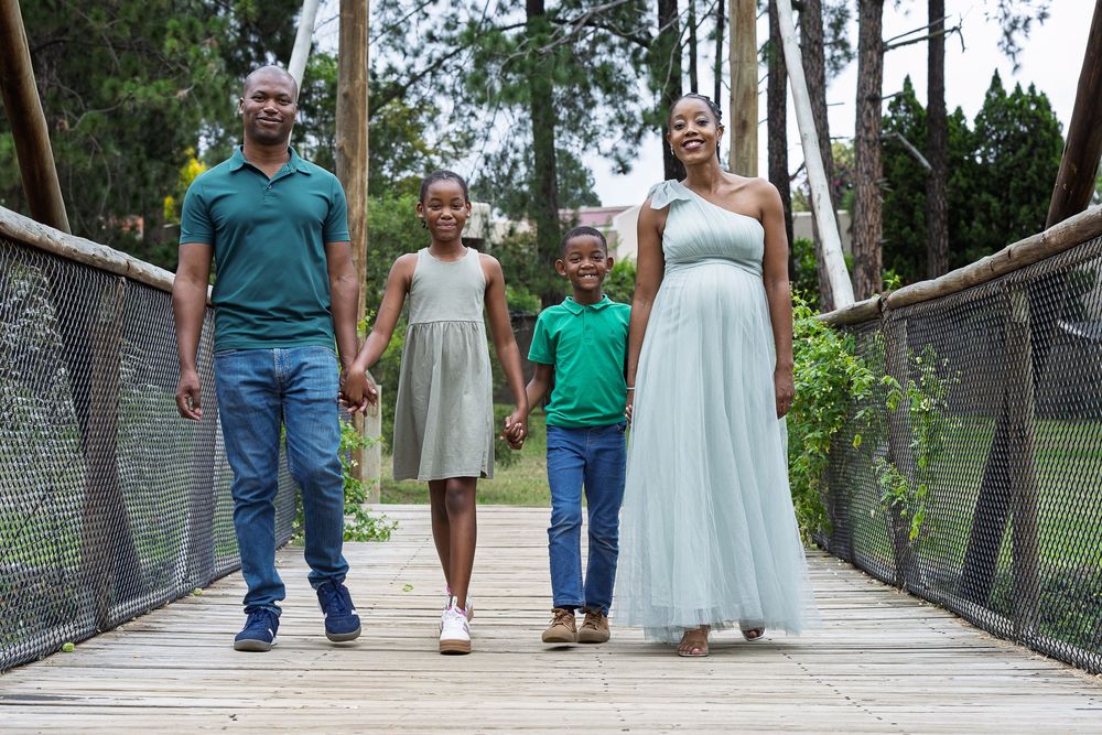 Family of four walking together on wooden bridge surrounded by trees.