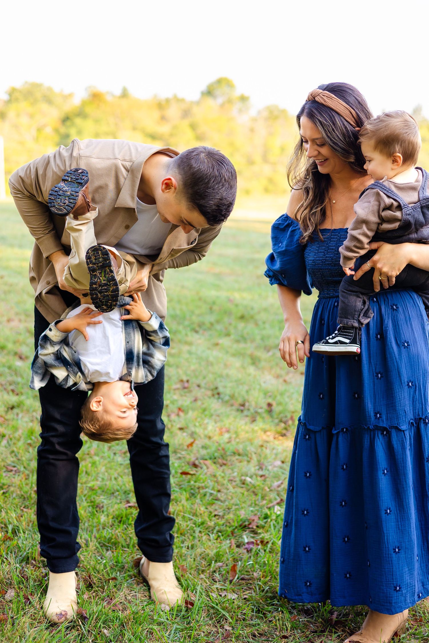 A couple in casual attire shares a tender moment in a sunlit grassy field during an outdoor photo session.