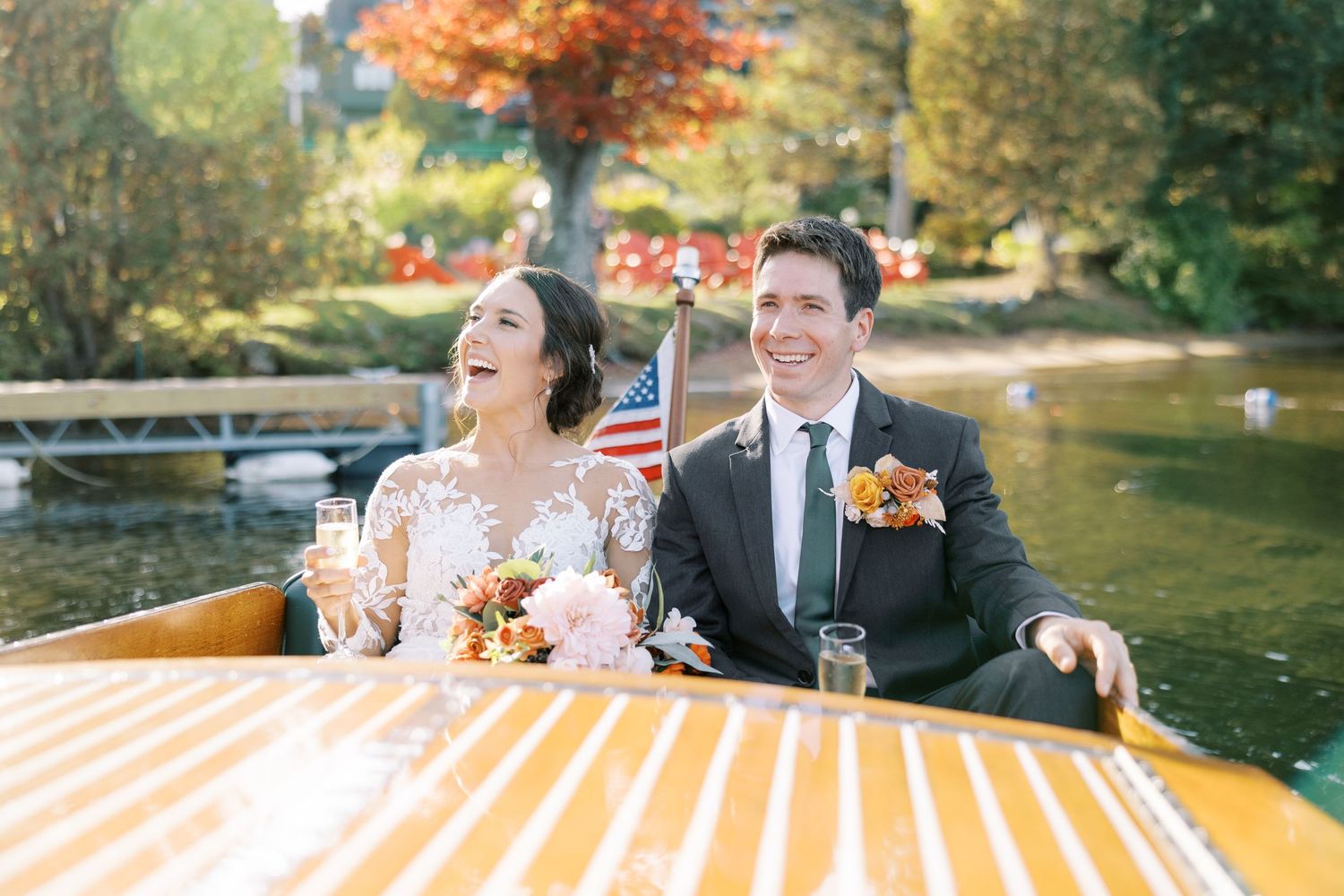 Newlyweds share a romantic moment in a Chris-Craft boat with colorful fall foliage in the background on Lake Placid.