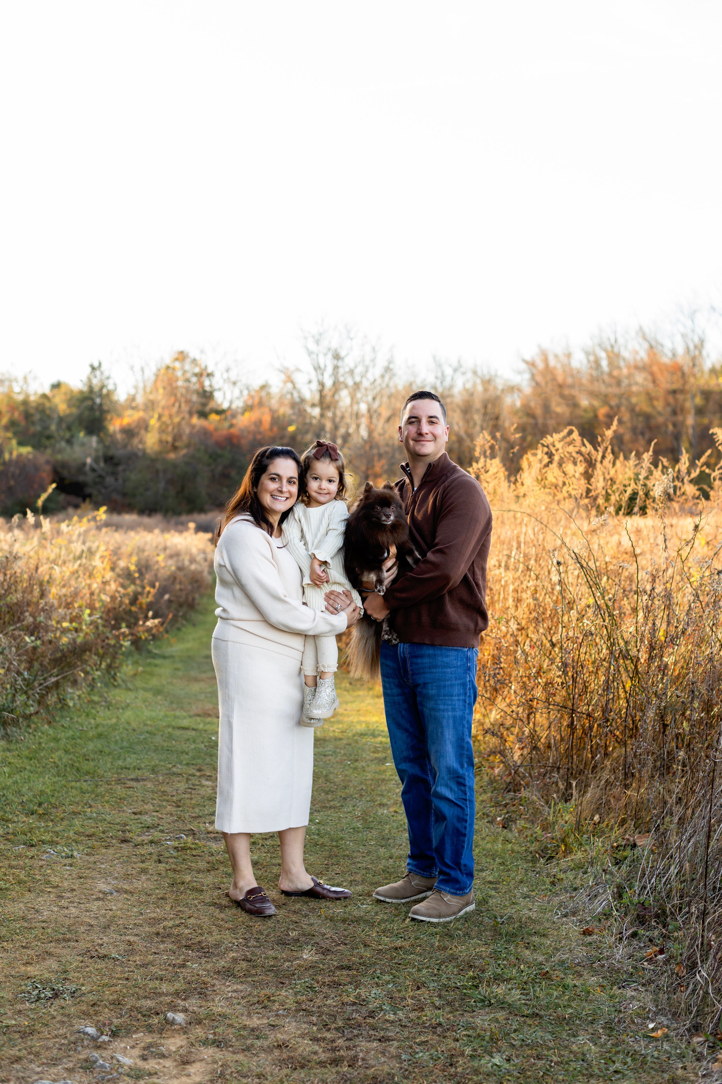 A family enjoying a warm autumn day together in a field with tall golden grass at sunset.