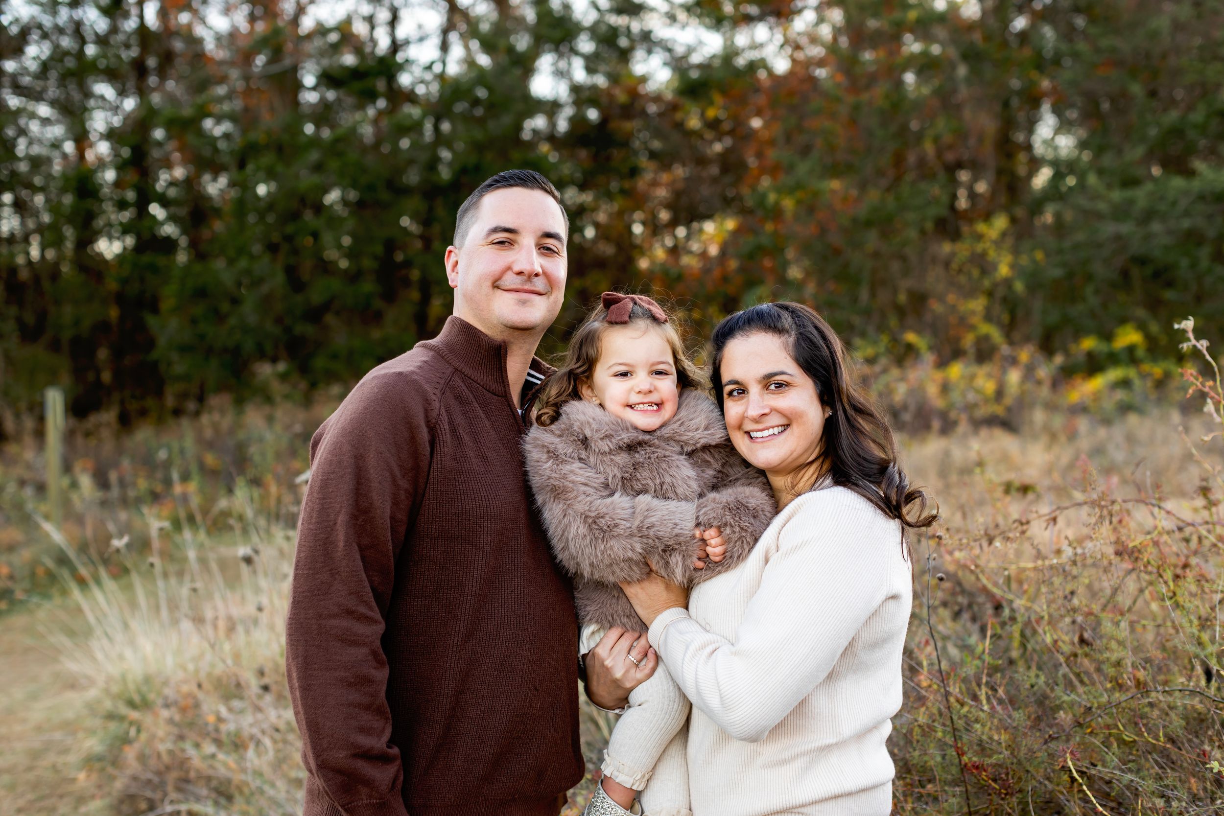A family enjoys a tender moment together during an outdoor autumn photoshoot in a rustic field setting.