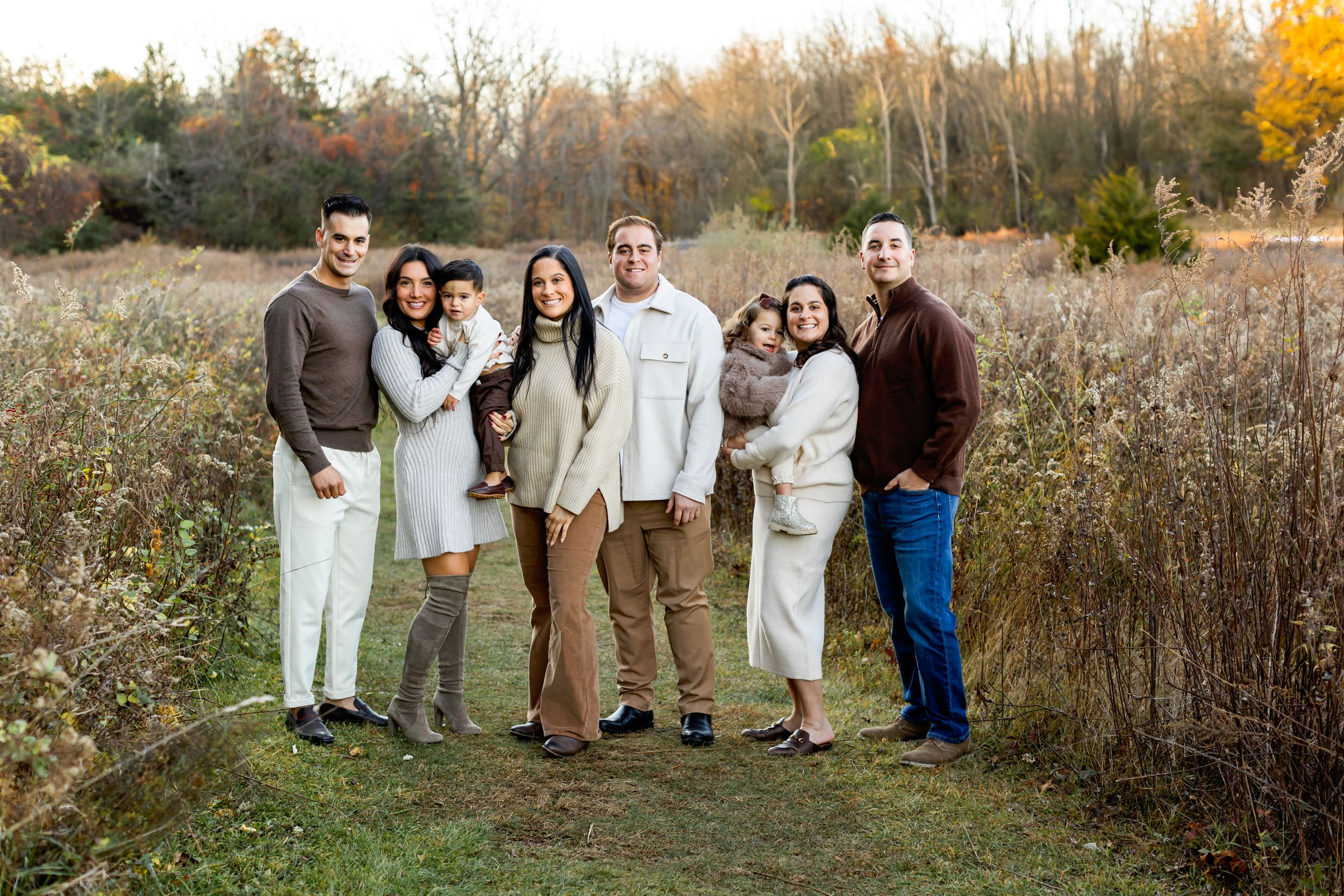 A group poses together in a natural outdoor setting with autumn foliage and tall grass in the background.