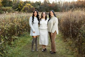A group in neutral-toned clothing walks together on a winding path through autumn fields at sunset.