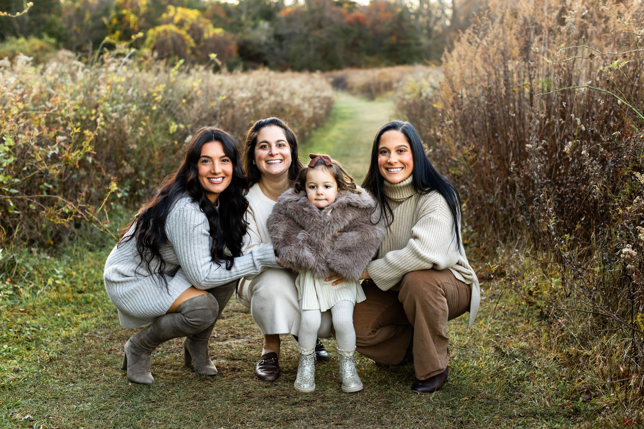 People sit together on the ground in a casual outdoor photoshoot with fall foliage and grass surrounding them.