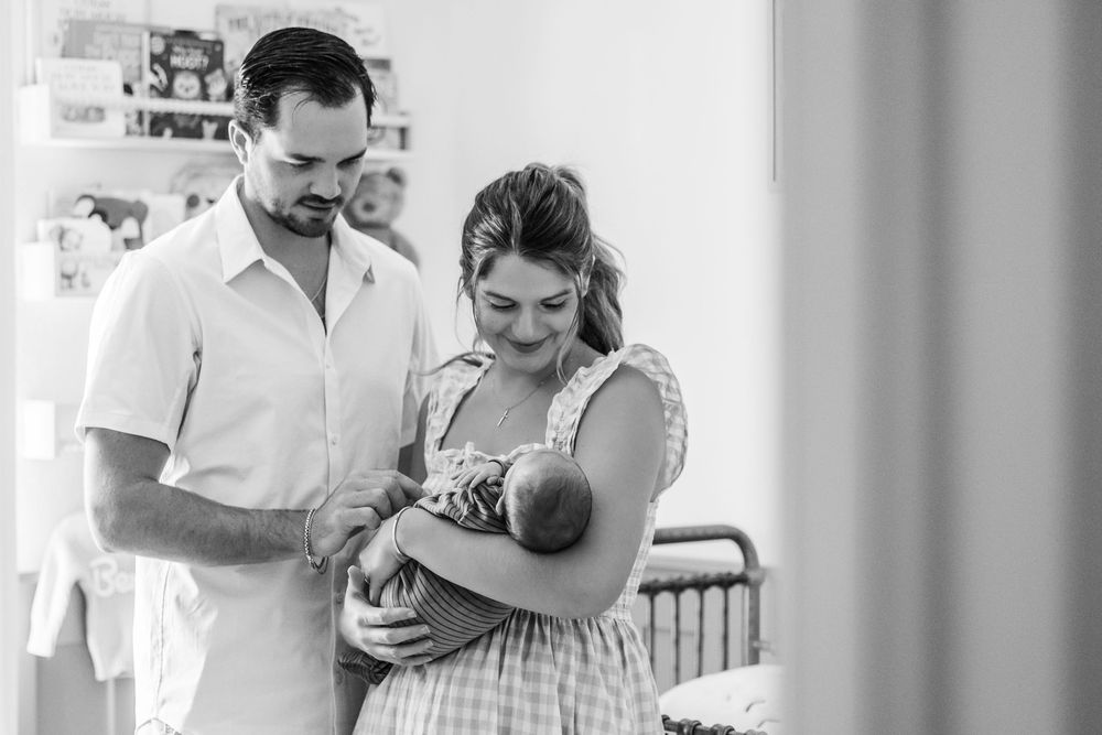 A black and white photograph shows a couple in a hospital room looking down lovingly at their newborn baby.