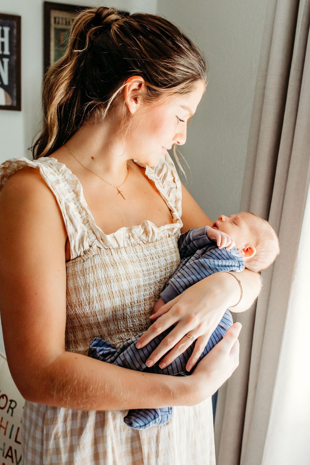 A mother in a floral dress holds and gazes lovingly at her newborn baby in a series of tender moments by a window.
