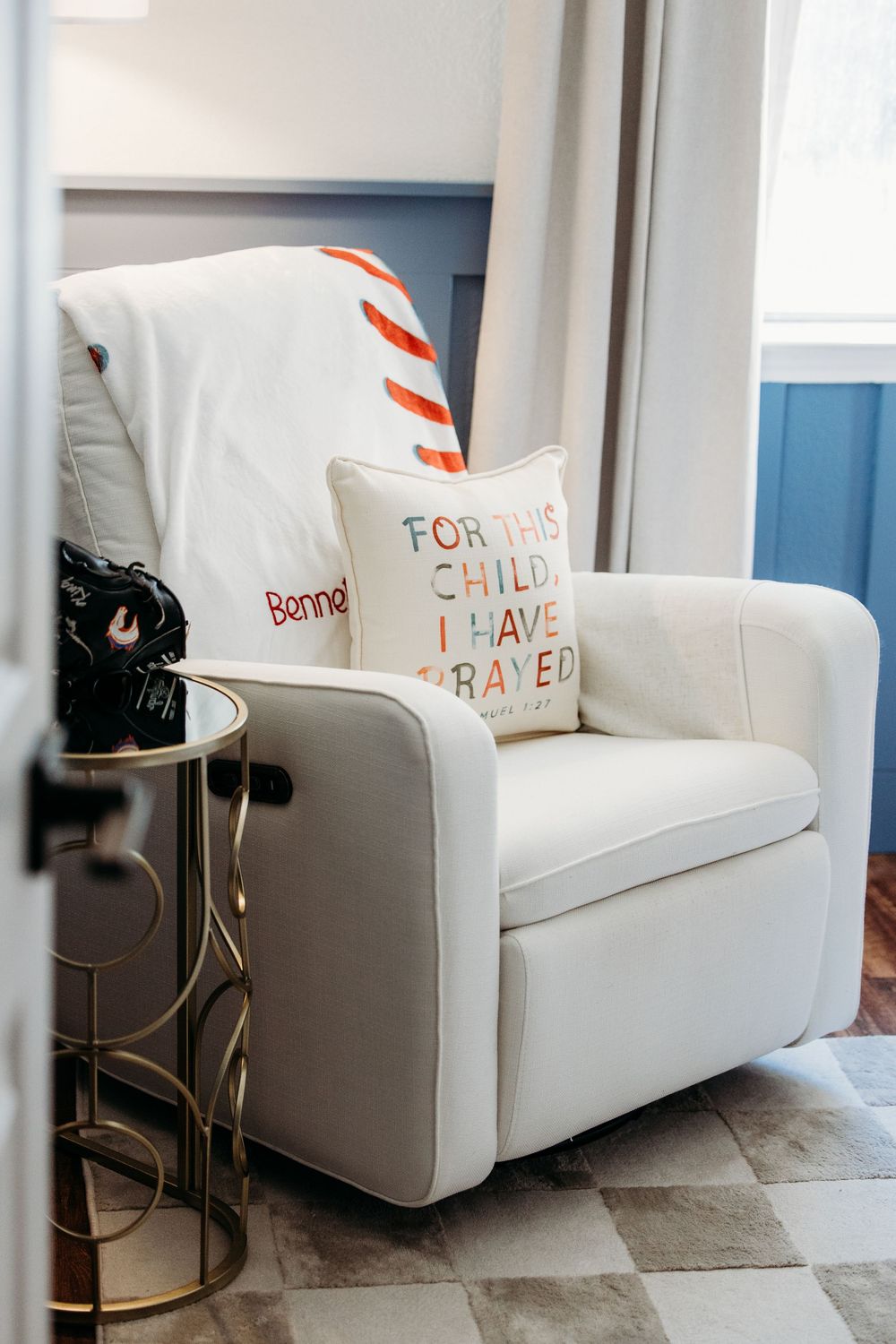 White glider rocking chair with decorative throw pillows sits against a blue wall in a modern nursery setting in Watauga