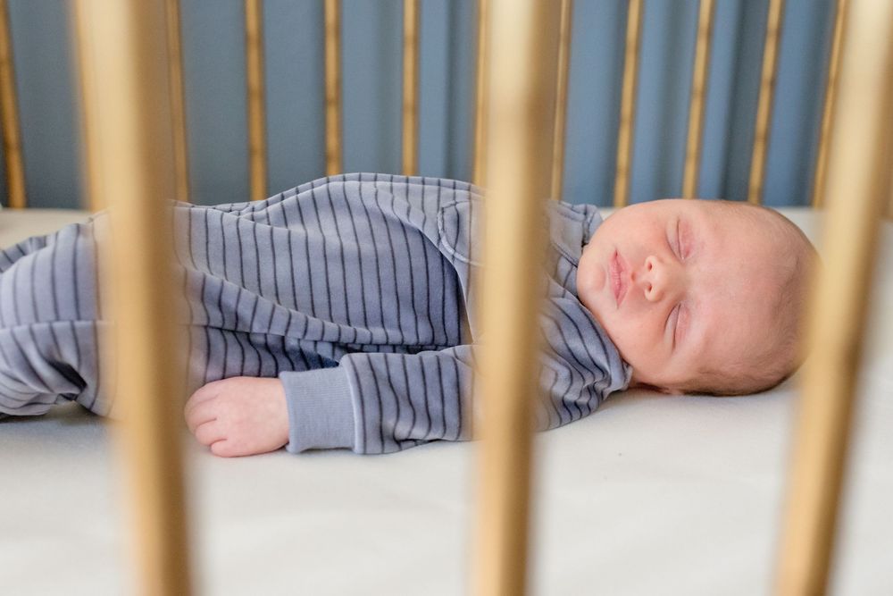 A sleeping baby in striped pajamas rests peacefully in a wooden crib viewed through the slats.