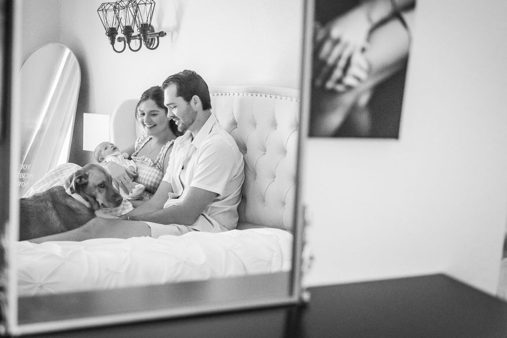 Black and white reflection in mirror shows family sitting together on bed reading in cozy bedroom interior.