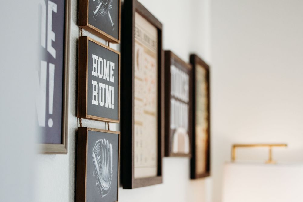 A gallery wall features black and white framed artwork and signs arranged in a clean, modern layout against a white wall.
