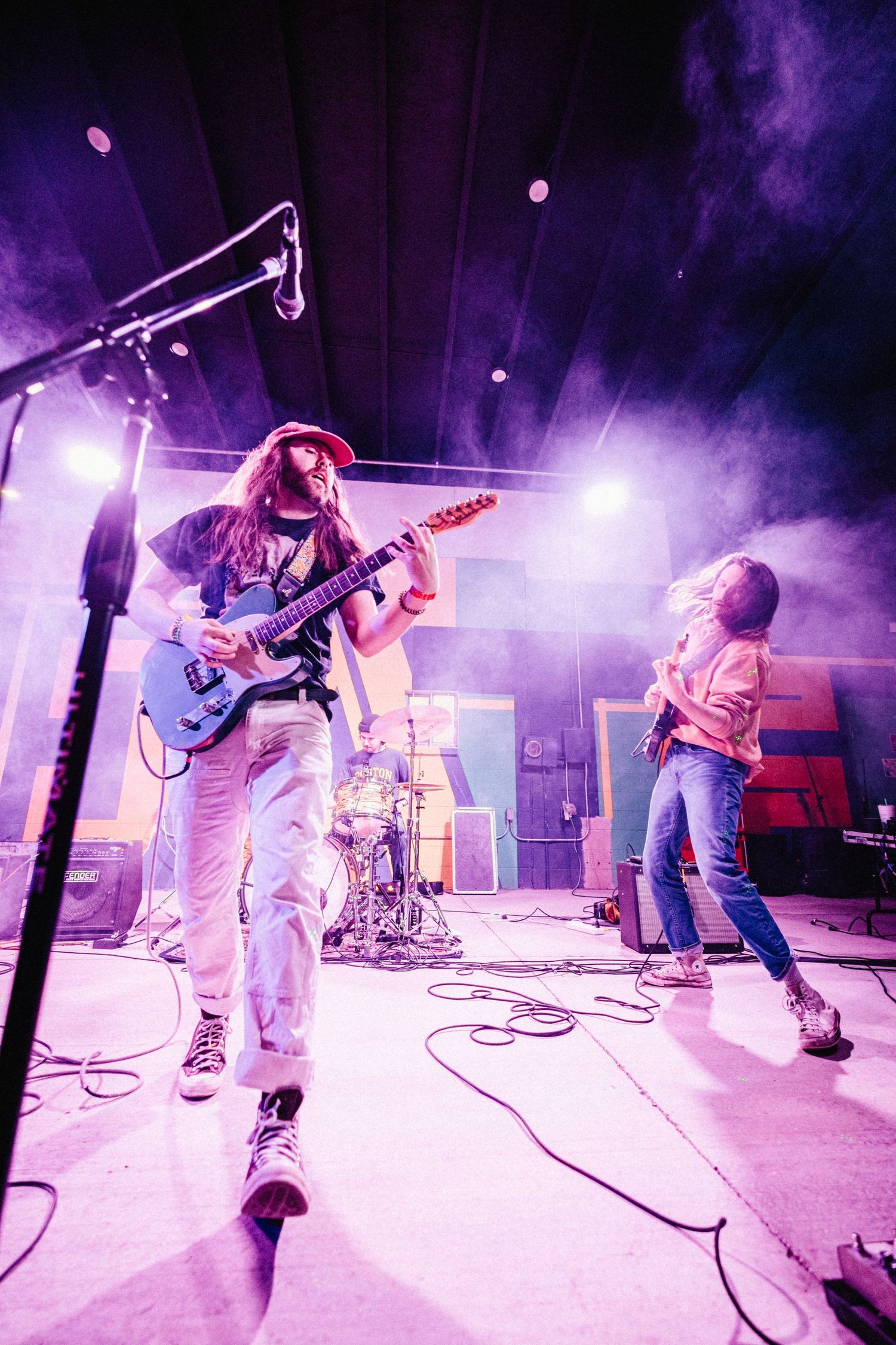 Band members perform on stage with purple lighting and fog effects during an energetic live concert performance.