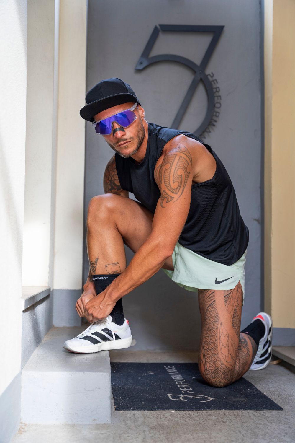 A man tying his shoes in a minimalist gym hallway; candid athletic lifestyle and fitness apparel photography.