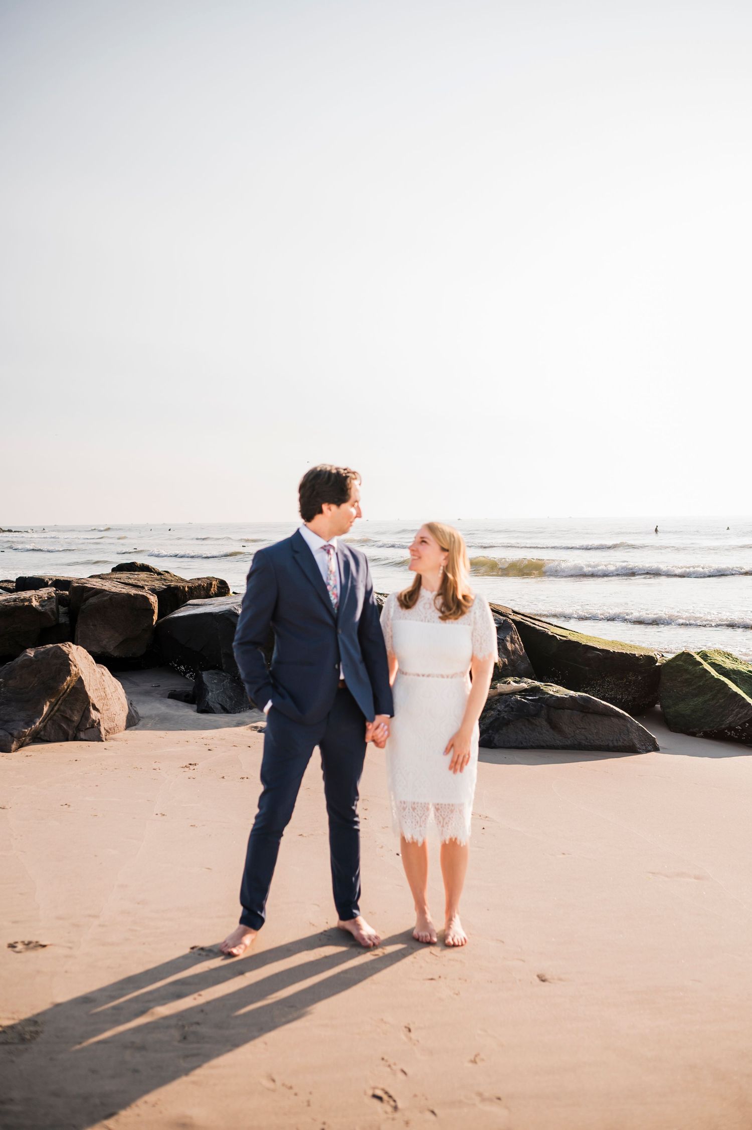 A couple walks along a scenic beach at sunset casting long shadows on the sand.