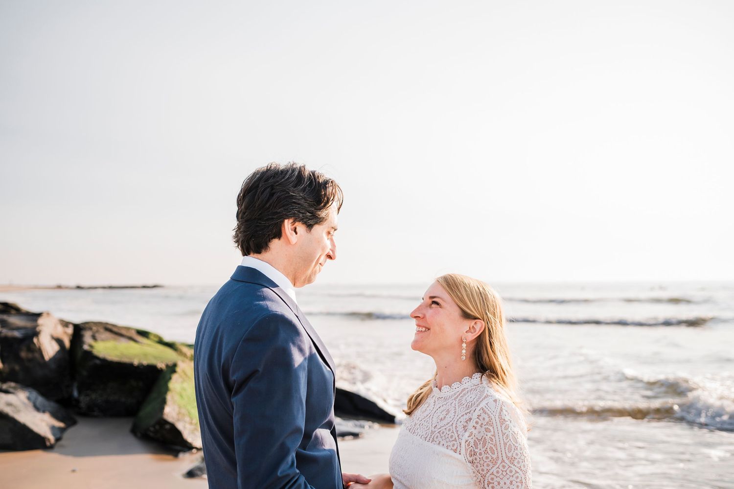 A romantic couple shares an intimate moment on a sandy beach during sunset with ocean waves in the background.
