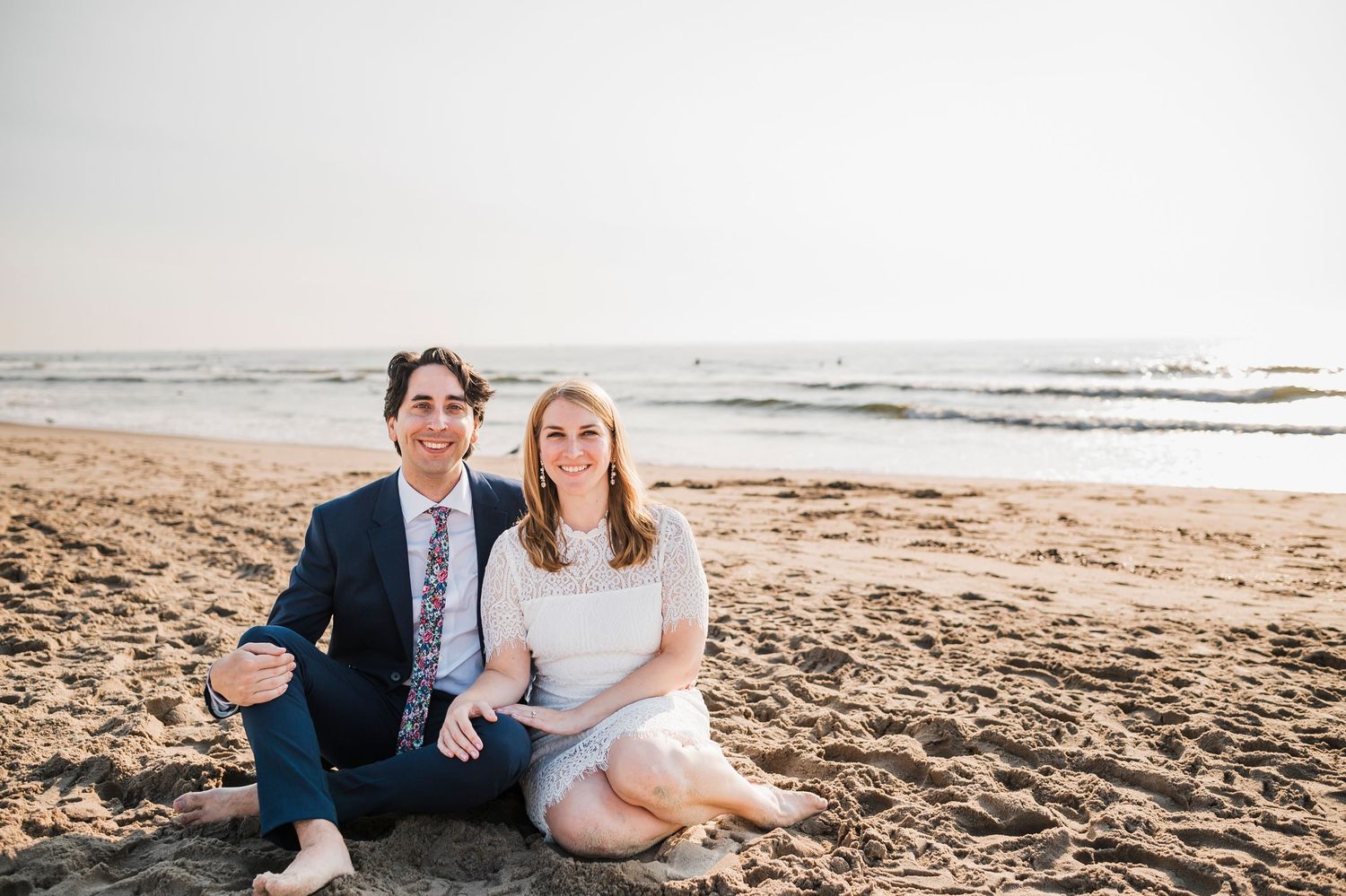 A couple sits together on a sandy beach at sunset enjoying a romantic moment by the ocean waves.