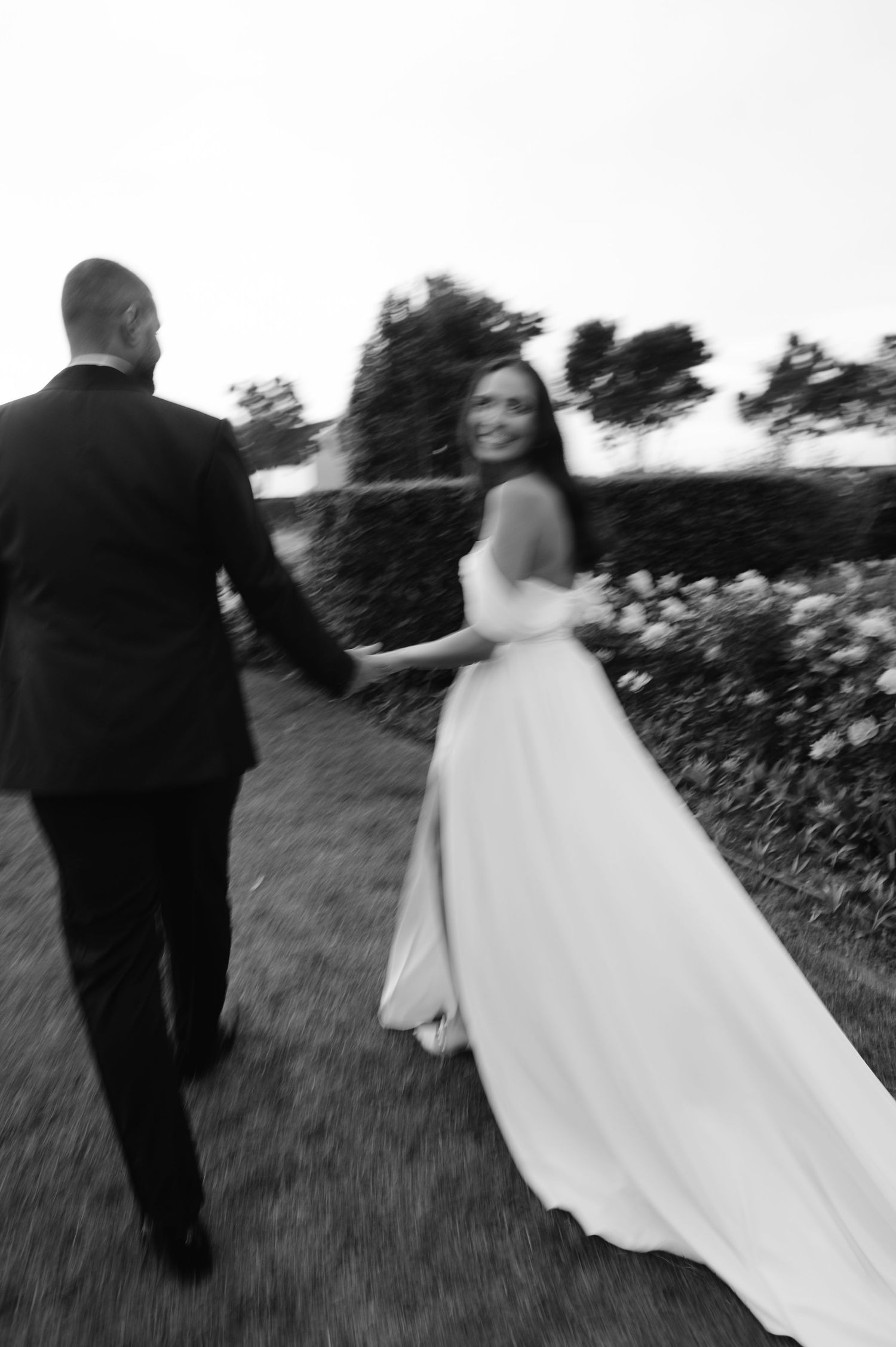 Black and white wedding photo series showing a couple walking together through a field in romantic motion blur style.