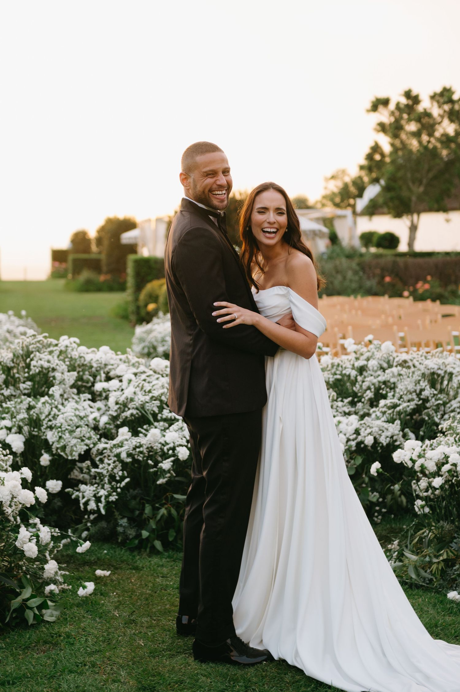 A couple shares joyful moments in a garden filled with blooming white flowers during golden hour.