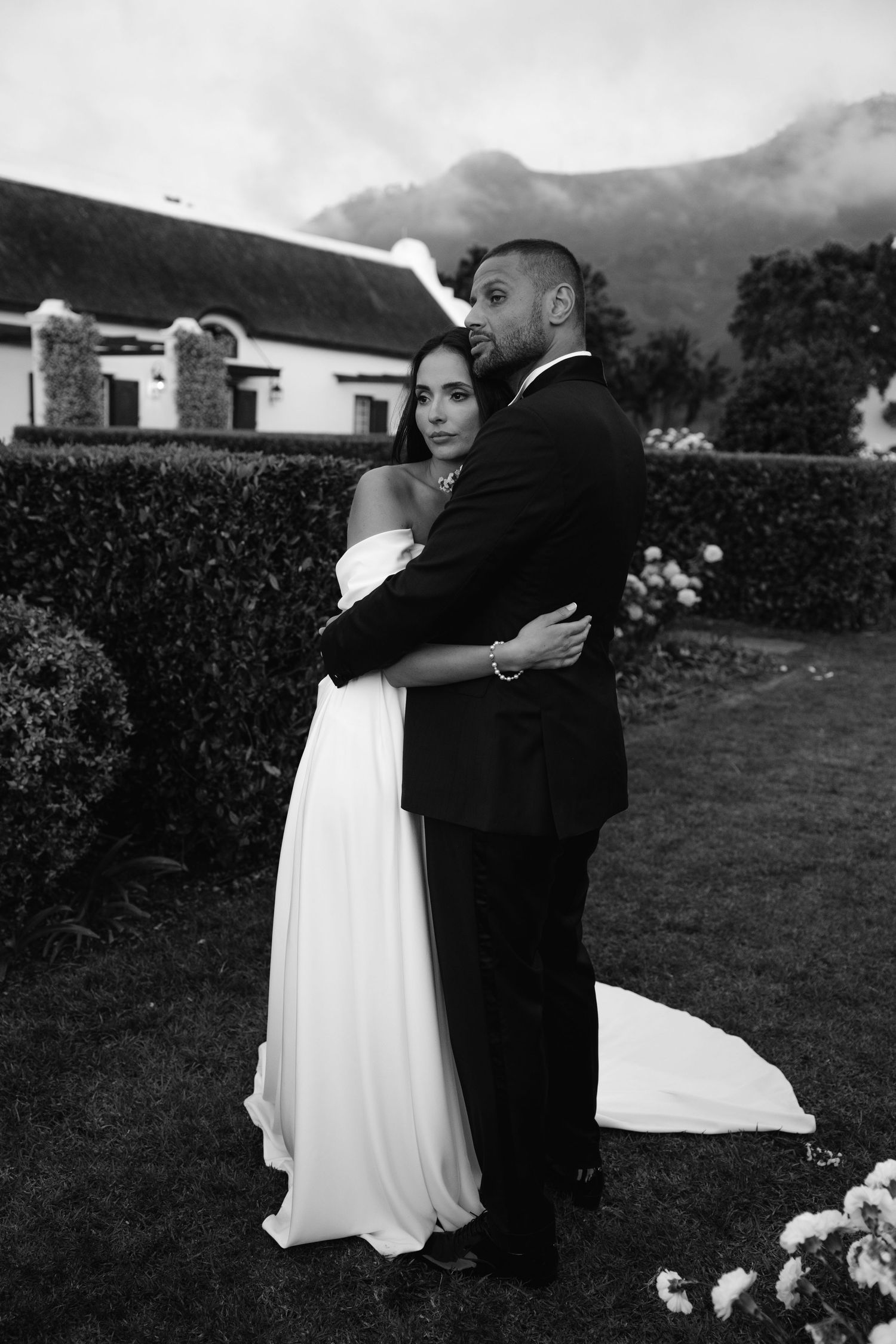 Black and white wedding photos show couple embracing outdoors with mountains and hedges in background.