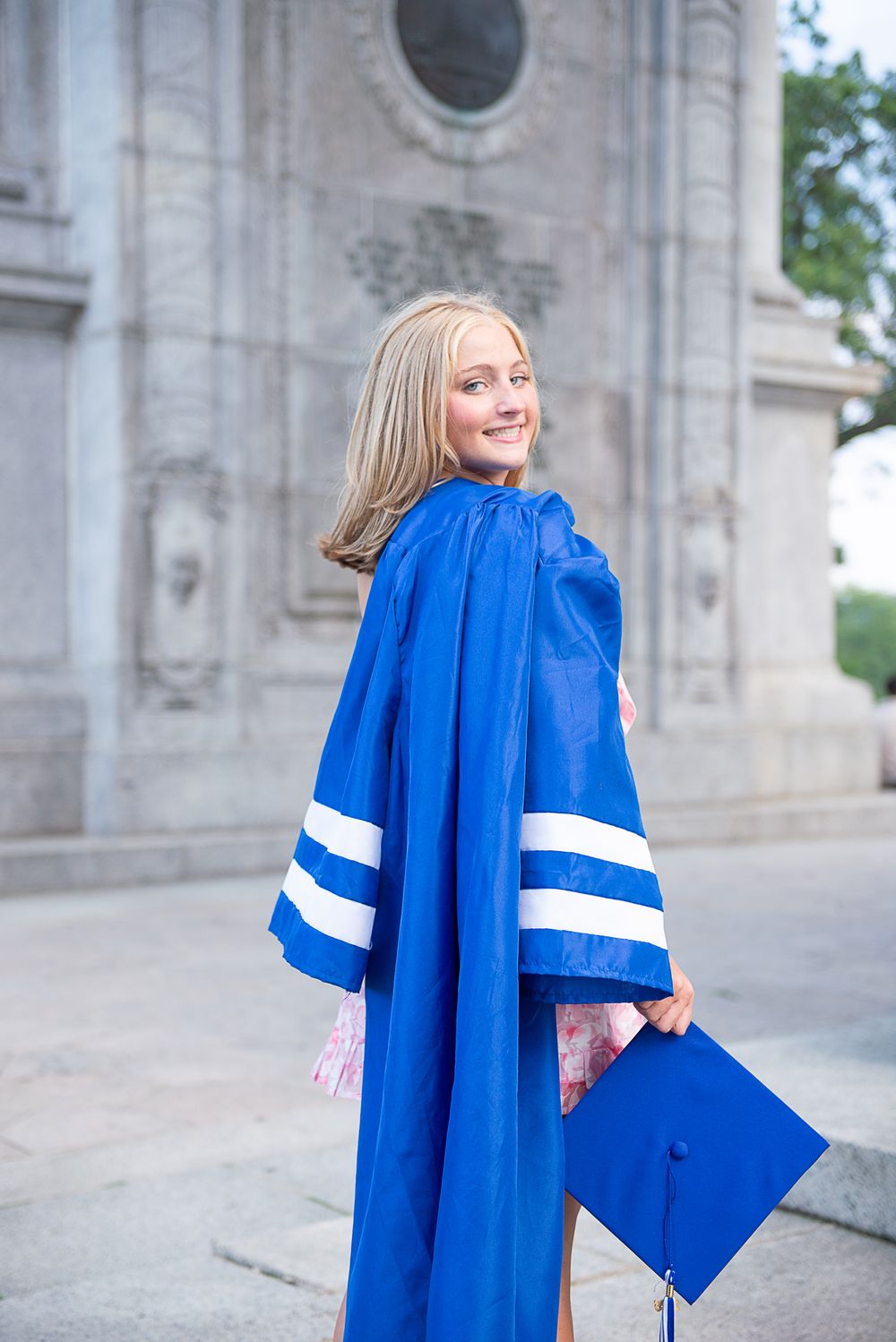 Graduate in bright blue academic regalia poses in front of stone building during graduation photoshoot.