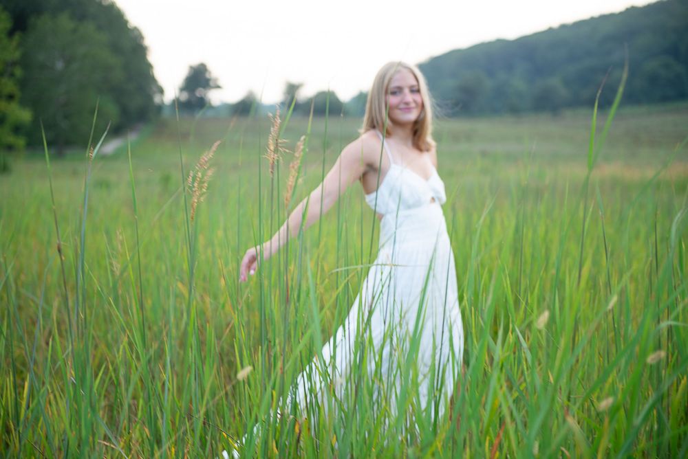 A person in a white dress walks through a lush green meadow on a sunny summer day.