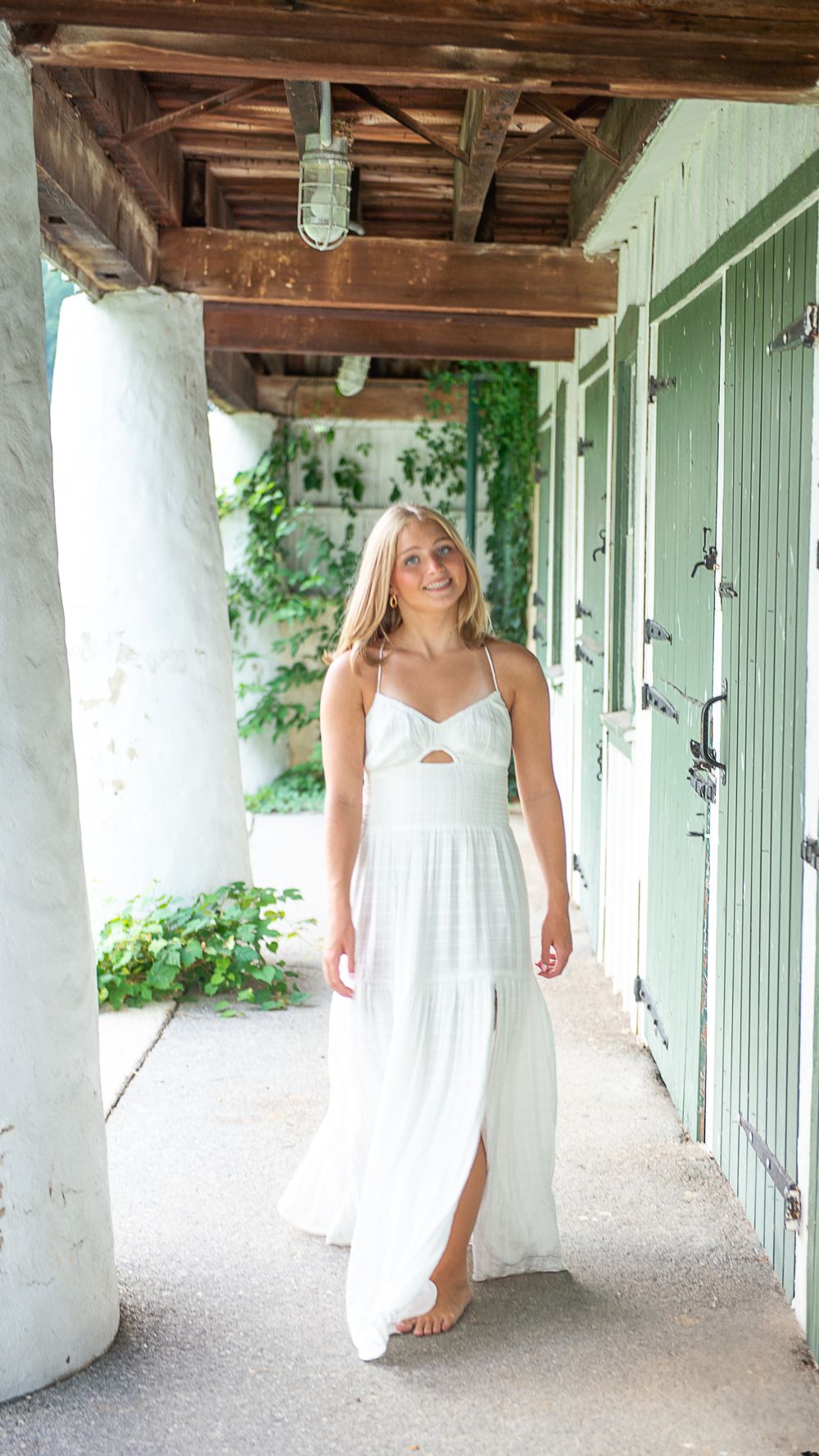 Woman in white dress walks through rustic covered porch with wooden beams and white columns.