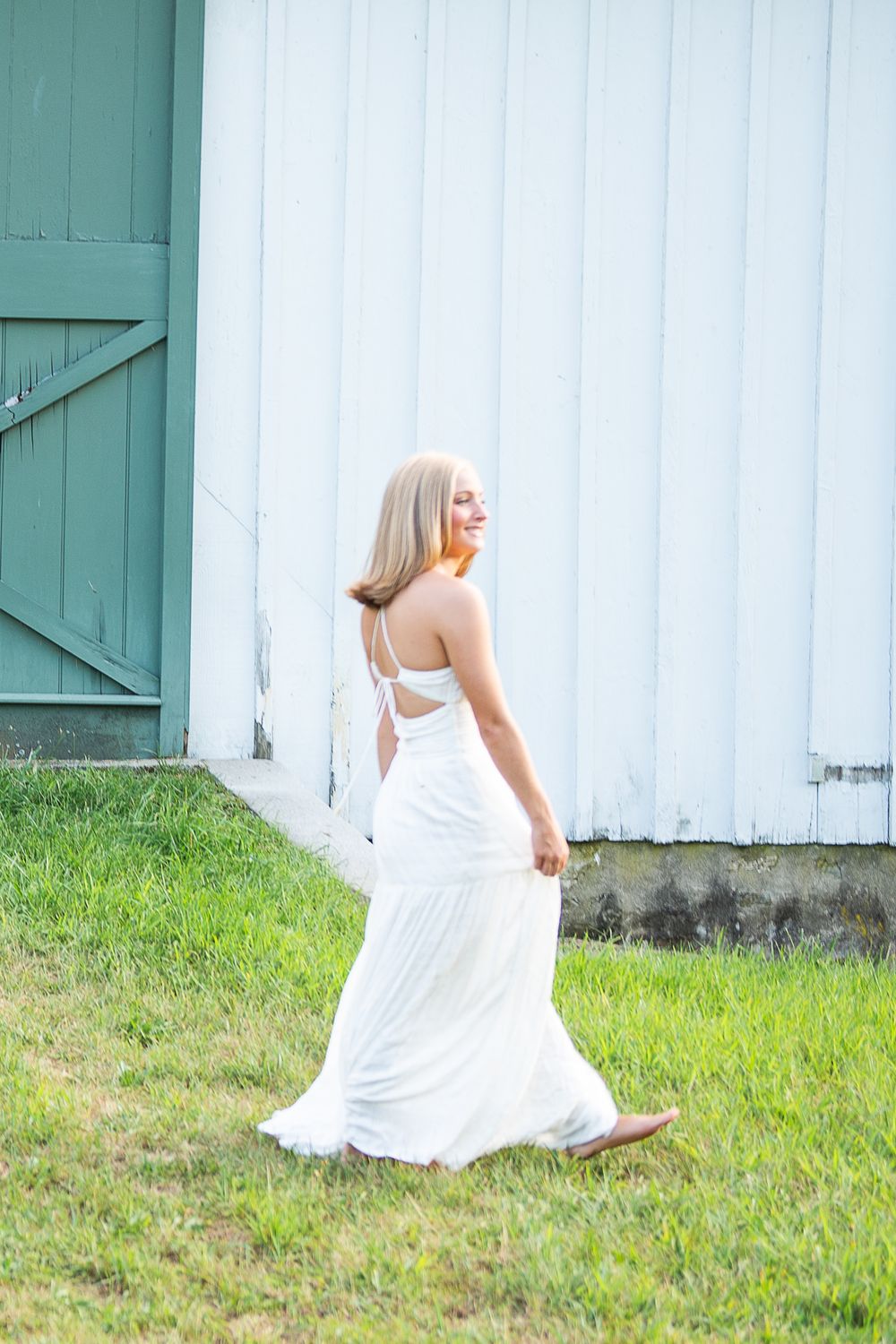 A person in a flowing white dress twirls gracefully on a grassy lawn beside a white building wall.