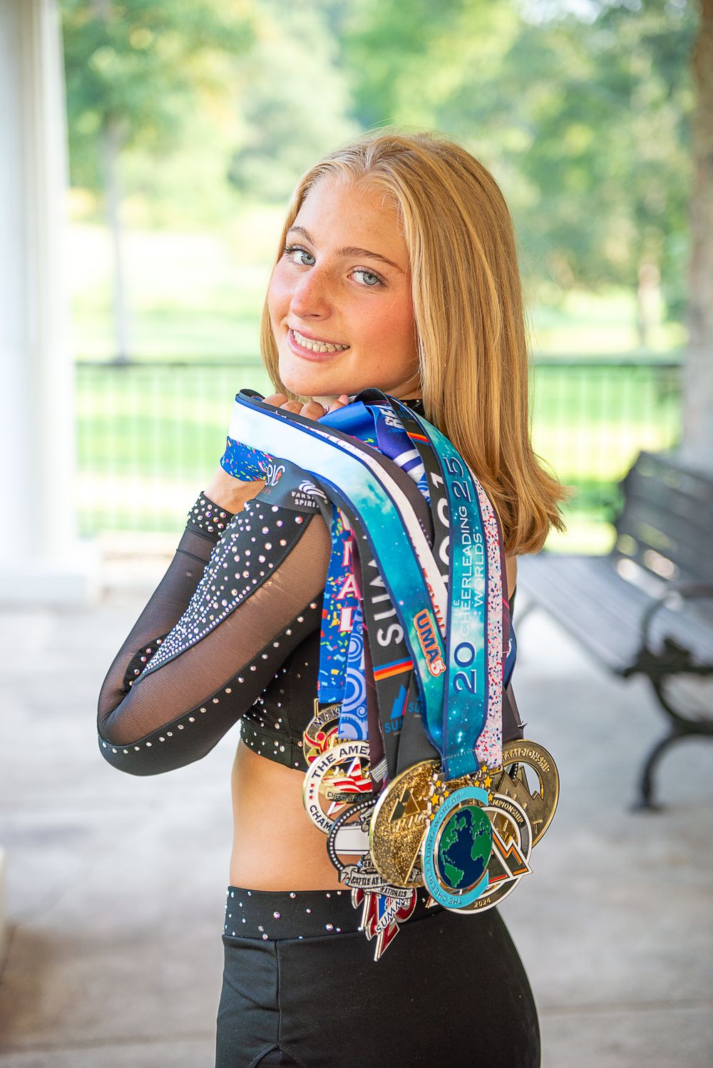 Athlete showing off collection of colorful race medals and ribbons while wearing black athletic wear on outdoor porch.